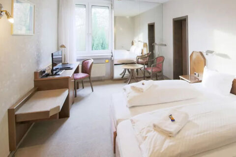 Hell eingerichtetes Hotelzimmer mit zwei Einzelbetten, Schreibtisch, St&uuml;hlen und gro&szlig;em Fenster im Hotel Kick.