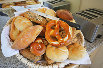 Frisches Br&ouml;tchen- und Brezenauswahl in einem Korb neben Toastern, Fr&uuml;hst&uuml;cksbuffet im Hotel Kick mit verschiedenen Brotsorten.