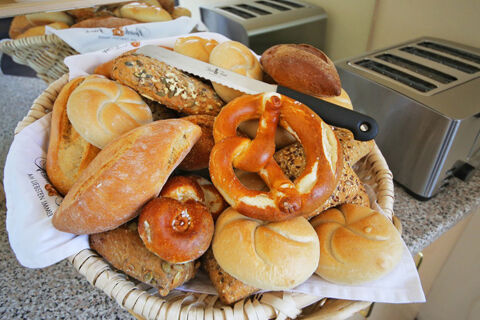 Frisches Br&ouml;tchen- und Brezenauswahl in einem Korb neben Toastern, Fr&uuml;hst&uuml;cksbuffet im Hotel Kick mit verschiedenen Brotsorten.