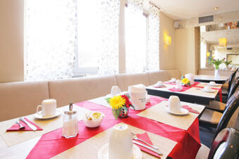 Helles und freundliches Fr&uuml;hst&uuml;ckszimmer mit gedeckten Tischen und dekorativen Blumen im Hotel Kick bei Tageslicht.
