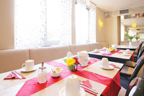 Helles und freundliches Fr&uuml;hst&uuml;ckszimmer mit gedeckten Tischen und dekorativen Blumen im Hotel Kick bei Tageslicht.