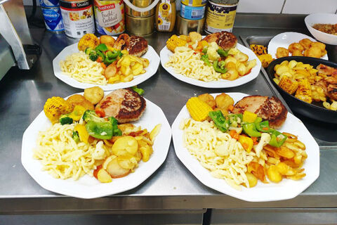 Vier Teller mit einer Mahlzeit aus Sp&auml;tzle, gebratenem Gem&uuml;se, Maiskolben und Frikadellen in der K&uuml;che von Hotel Kick.