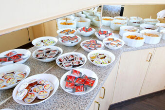 Hotel Kick Fr&uuml;hst&uuml;ckstheke mit verschiedenen Marmeladen, Honigportionen und mehreren Schalen voller Cerealien und Cornflakes.