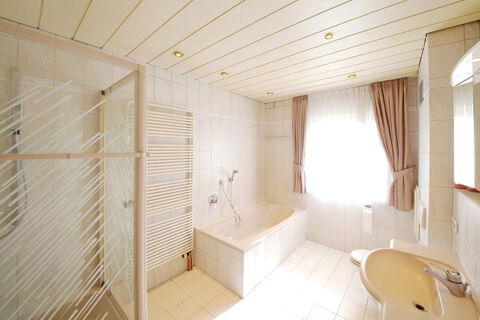 Helles, modern gefliestes Badezimmer mit Badewanne, Dusche, Waschbecken und Fenster mit Gardinen im Hotel Kick.