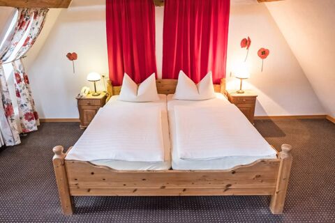 Gem&uuml;tliches Schlafzimmer mit Holzbett, wei&szlig;en Bettdecken und roten Gardinen im Marktplatzhotel u. Bistrorant Tafelspitz mit Blumenmuster Vorh&auml;ngen.