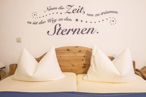 Gem&uuml;tliches Doppelbett mit wei&szlig;en Kissen und Holzkopfteil in einem Zimmer des Marktplatzhotel u. Bistrorant Tafelspitz mit einer Wanddekoration als Zitat.