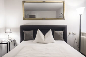 Bed with black headboard, two gray and two white pillows, bedside lamps, and mirror in Marktplatzhotel u. Bistrorant Tafelspitz