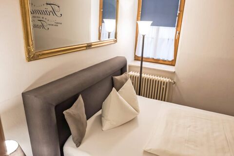 Gem&uuml;tliches Schlafzimmer mit einem dunkelgrauen gepolsterten Kopfteil, dekorativen Kissen und einem Fenster im Marktplatzhotel u. Bistrorant Tafelspitz.
