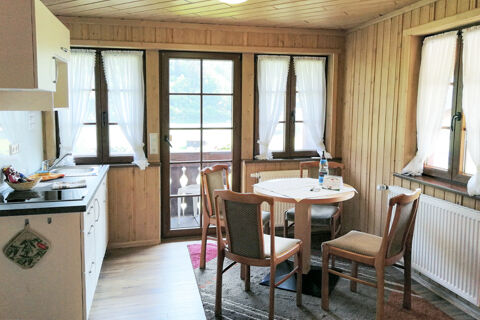 Gem&uuml;tliche K&uuml;che mit Holzvert&auml;felung, rundem Tisch und Fenster mit wei&szlig;en Gardinen im Bauernhof W&auml;ldebauernhof.
