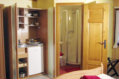Kleine K&uuml;chenzeile mit K&uuml;hlschrank und Geschirr neben einem Badezimmer mit Dusche in einem rustikalen Zimmer des Bauernhof W&auml;ldebauernhof.