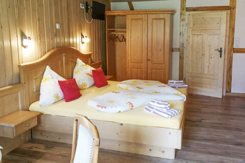 Gem&uuml;tliches Zimmer im Bauernhof W&auml;ldebauernhof mit hellem Holzdekor, Doppelbett und roten Kissen f&uuml;r behaglichen Komfort.