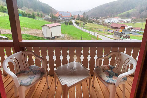Blick von einem holzgerahmten Balkon mit zwei wei&szlig;en St&uuml;hlen und kleinem Tisch auf gr&uuml;ne Wiesen und H&auml;user in der Ferne beim Bauernhof W&auml;ldebauernhof.