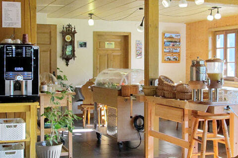 Hell eingerichteter Fr&uuml;hst&uuml;cksraum mit Holzm&ouml;beln, Buffetwagen und Kaffeeautomat im Bauernhof W&auml;ldebauernhof mit viel Tageslicht.