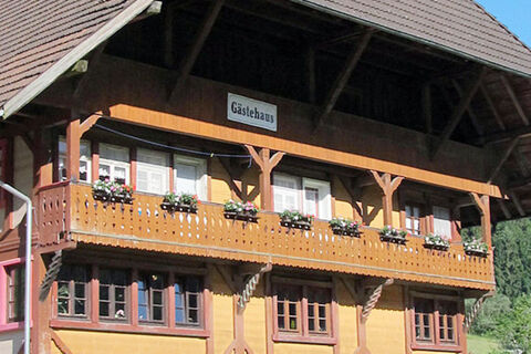 Fassade des G&auml;stehauses mit Balkon und Blumen dekoriert, Teil des Bauernhof W&auml;ldebauernhof in l&auml;ndlicher Umgebung bei Sonnenschein.