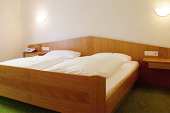 Schlicht eingerichtetes Hotelzimmer im Hotel Landgut Burg mit einem Doppelbett, Holzm&ouml;beln und gr&uuml;nem Teppichboden.