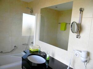 Modernes Badezimmer im Hotel Landgut Burg mit Badewanne, Duschvorrichtung, gro&szlig;em Spiegel und Handt&uuml;chern in gr&uuml;ner Farbe.
