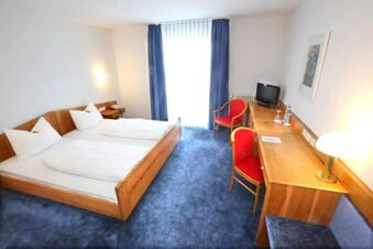 Helles Hotelzimmer mit Doppelbett, blauem Teppich und roten St&uuml;hlen im Hotel Landgut Burg, gem&uuml;tlicher Arbeitsbereich