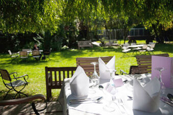 Sonnige Au&szlig;enbestuhlung mit eingedeckten Tischen und wei&szlig;en Servietten im Garten des Hotel Landgut Burg.