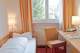 Helles Hotelzimmer mit Einzelbett, Schreibtisch und Fenster mit Blick auf B&auml;ume im Hotel Landgut Burg.