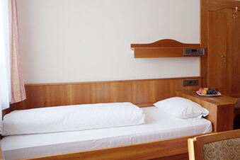 Ein einfach eingerichtetes Einzelzimmer mit Holzm&ouml;beln, wei&szlig;er Bettw&auml;sche und einem Obstteller im Hotel Landgut Burg.