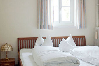 Hell eingerichtetes Schlafzimmer mit einem Holzbett, wei&szlig;en Bettdecken und einem Fenster mit Vorh&auml;ngen im Hotel Landgut Burg.