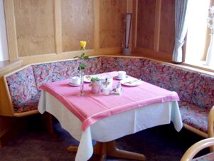 Gem&uuml;tliche Sitzecke mit buntem Polster und gedecktem Tisch mit rosa Tischdecke im Gasthof Schwarzer Adler.