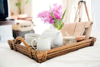 Ein Tablett mit Teekanne, Tassen, Milchkanne, Dose und rosa Blumen steht auf einem Bett im gem&uuml;tlichen Zimmer des Gasthofs Schwarzer Adler.