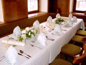 Eleganter und festlich gedeckter Tisch mit wei&szlig;en Servietten, Blumenarrangements und Men&uuml;karten im Gasthof Schwarzer Adler.