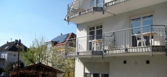 Au&szlig;enansicht des Gasthofs Schwarzer Adler mit Balkonen und Garten in einer sonnigen Wohngegend, umgeben von B&auml;umen und Nachbarh&auml;usern.