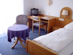 Helles Hotelzimmer mit Bett, Schreibtisch, St&uuml;hlen und kleinem Fernseher im Gasthof Schwarzer Adler, schlicht und funktional eingerichtet.