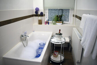 Bathroom of Pension Lachmann with a white bathtub filled with foam, decorative plants, and a small table with champagne and glasses