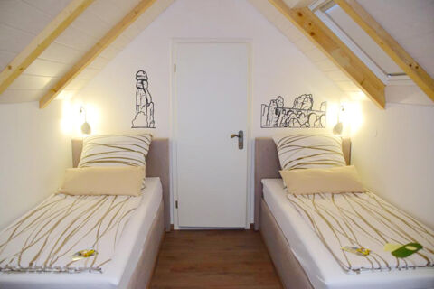 Two single beds with striped bedding and beige pillows in a white attic room with wooden beams at Pension Lachmann