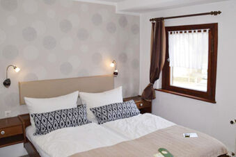 Double bed with white and patterned pillows in a room with brown curtains and polka dot wallpaper at Pension Lachmann