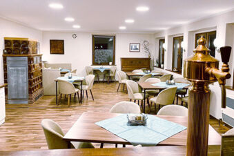 Dining area with wooden tables and beige chairs around them at Pension Lachmann, illuminated by ceiling lights
