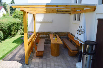 Outdoor wooden seating area with benches, table, umbrella, and heater under a wood-paneled roof at Pension Lachmann