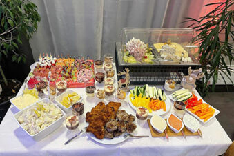 Buffet table at Pension Lachmann with assorted salads, fried meat, vegetable sticks, cheese under a transparent cover, and creamy dips