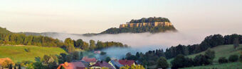 Foggy valley landscape with houses in the foreground and a flat-topped mountain in the background near Pension Lachmann