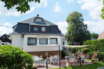 Pension Lachmann white building with outdoor seating area featuring plastic chairs and tables under a white canopy on a sunny day