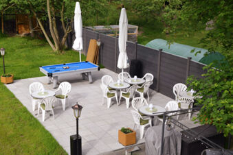 Outdoor seating area with white plastic tables and chairs, pool table with blue felt, and umbrellas at Pension Lachmann