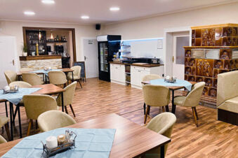 Dining area at Pension Lachmann with several tables covered in blue cloths and numerous beige chairs on wooden floors