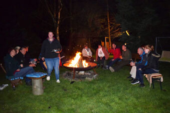 A group of people sitting and standing around a fire pit at night on a grassy area at Pension Lachmann