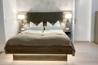 Modern double bed with brown bedding and multiple pillows in a room at Pension Lachmann with wall lamps and wooden flooring