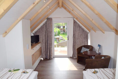 Bright attic room at Pension Lachmann with two beds, wooden beams, a TV cabinet, and a small seating area by glass door