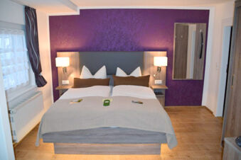 Modern bedroom at Pension Lachmann with a double bed, purple accent wall, wooden floor, bedside tables, and wall lamps