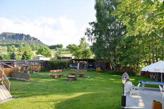 Outdoor seating area with wooden benches and fire pit on grass, patio with chairs and umbrella at Pension Lachmann