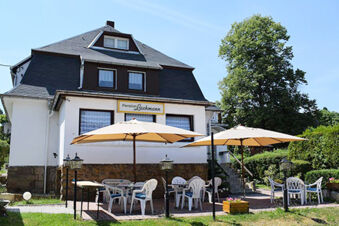 White two-story building with sign Pension Lachmann and outdoor seating area with tables and umbrellas on grass