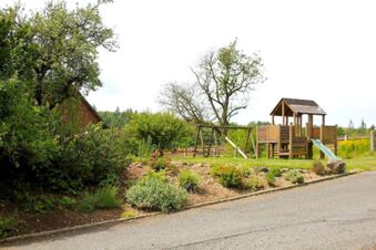Spielplatz im Garten mit Rutsche und Schaukel vor einer gr&uuml;nen Landschaft beim Landgasthof Haueis mit B&auml;umen und Blumenbeeten
