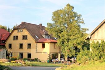 Au&szlig;enansicht des Landgasthof Haueis mit Gartenbereich, vielen G&auml;sten sitzen an Tischen unter einem gro&szlig;en Baum.
