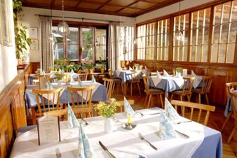 Hell eingerichteter Restaurantbereich mit Holzst&uuml;hlen und blau-wei&szlig;en Tischdecken im Landgasthof Haueis mit Tageslicht von gro&szlig;en Fenstern.