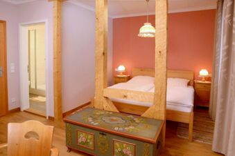 Gem&uuml;tliches Schlafzimmer mit Holzm&ouml;beln und Deko im Landgasthof Haueis, inklusive Blick ins angrenzende Badezimmer mit Dusche.